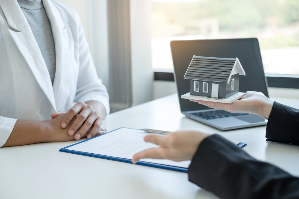 A real estate agent with a House model is talking to clients