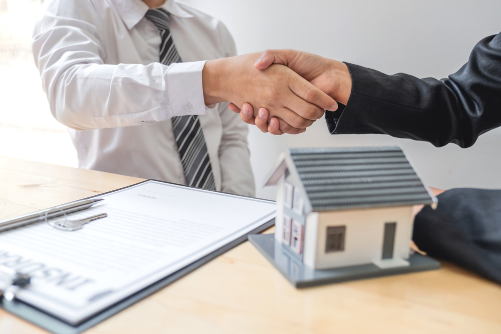 person and mortgage broker shake hands behind small model of house